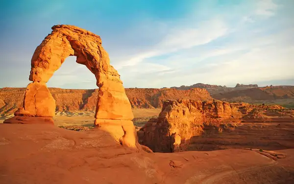 The red-rock Delicate Arch frames a landscape of red and orange cliffs in Utah