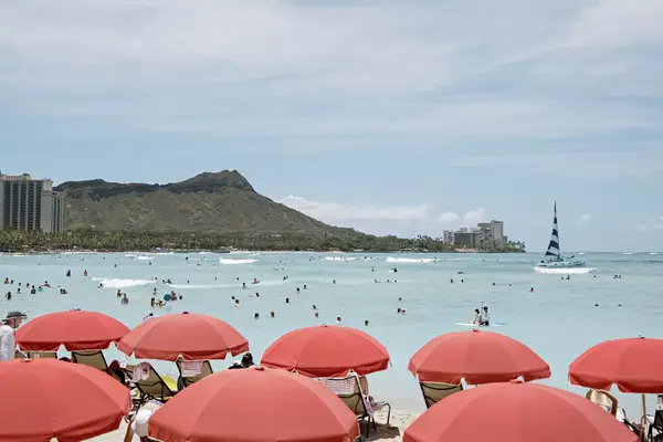 Red umbrellas on a beach in Hawaii, with Diamond Head in the distance