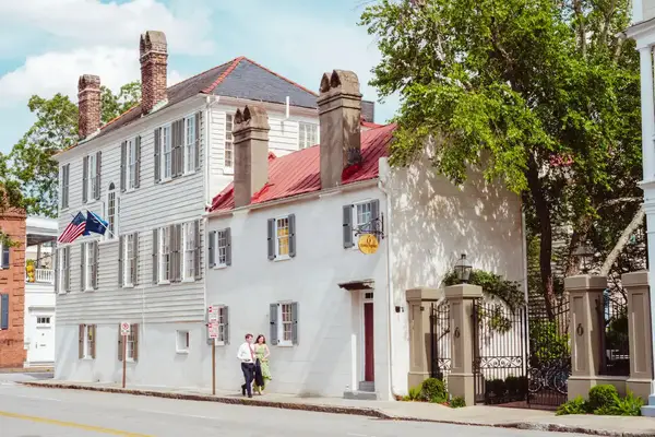 A couple walking past a white building with blue shutters.