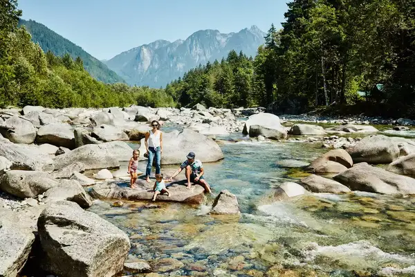 Smiling and laughing family hanging out on rock in river while on summer vacation