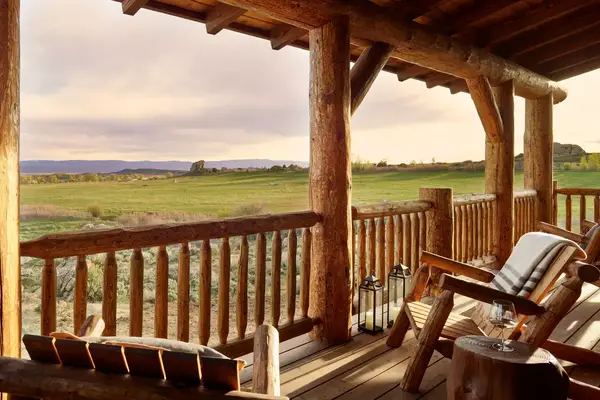 Rustic wooden porch overlooking an open landscape with chairs and a small table