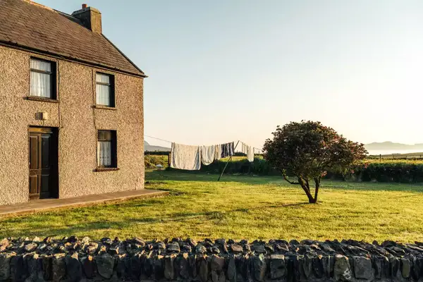 Stone cottage with drying laundry in a yard, countryside setting with a stone wall and scenic landscape