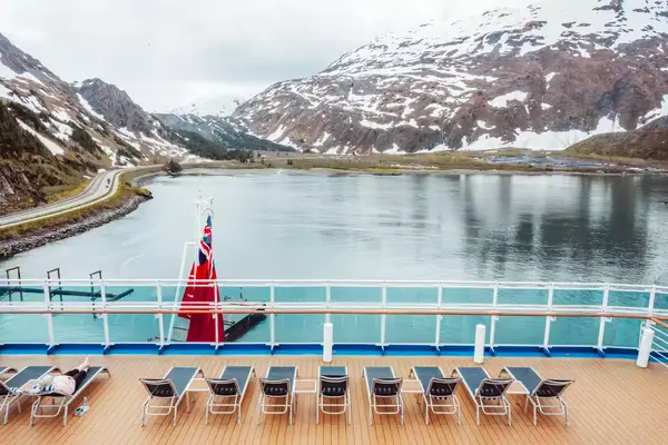 Deck chairs on a cruise ship facing icy mountains and a calm fjord under a cloudy sky