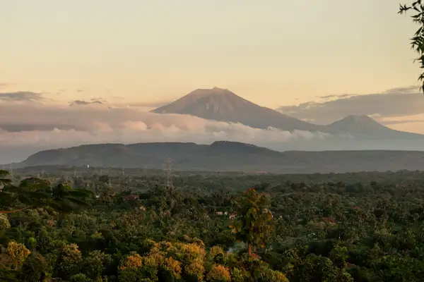A distant view of a mountain with clouds, surrounded by forested landscape