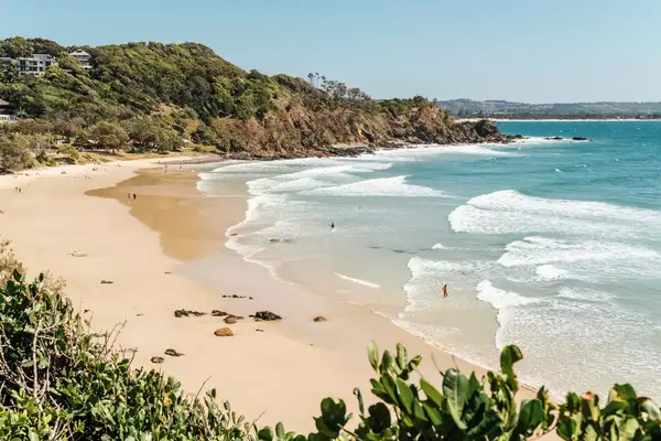 A scenic view of a beach with gentle waves, surrounded by greenery and distant cliffs