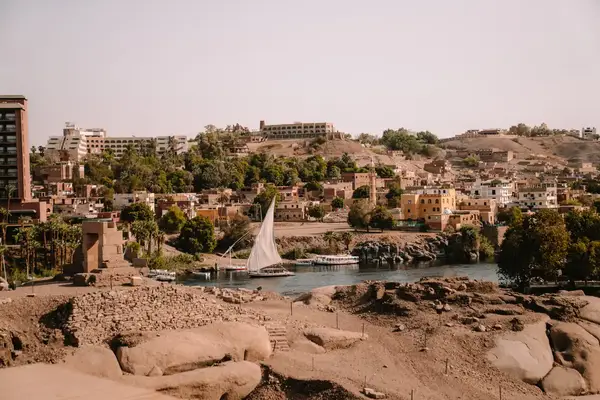 A sailboat on a riverbank with a town and buildings in the background