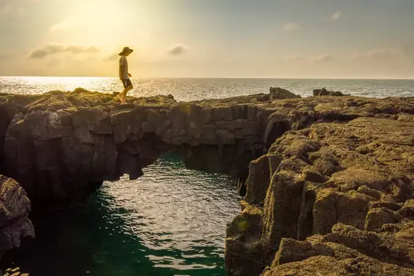 Person walking on a rocky outcrop near an ocean at sunset