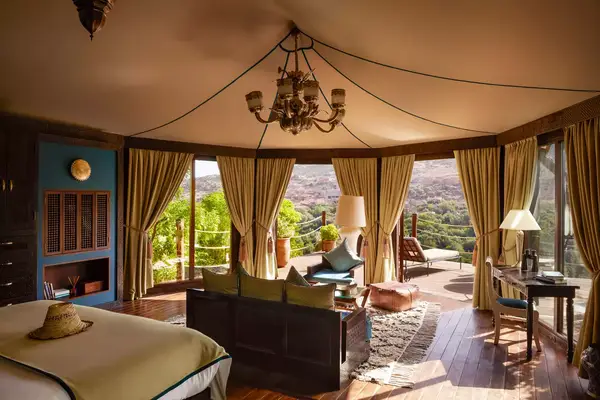 A luxurious suite with a view of the outdoor terrace and greenery, featuring a spacious bed and seating area