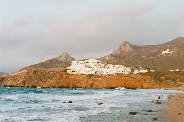 A coastal village on a hillside near the sea with mountains in the background