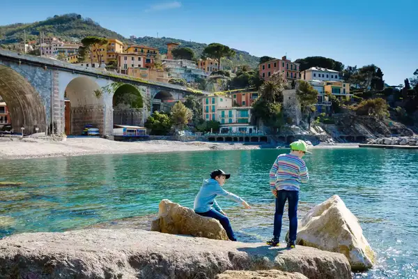 Two little kids boys climbing on beach stones of Mediterranean sea in Liguria region, Italy. 