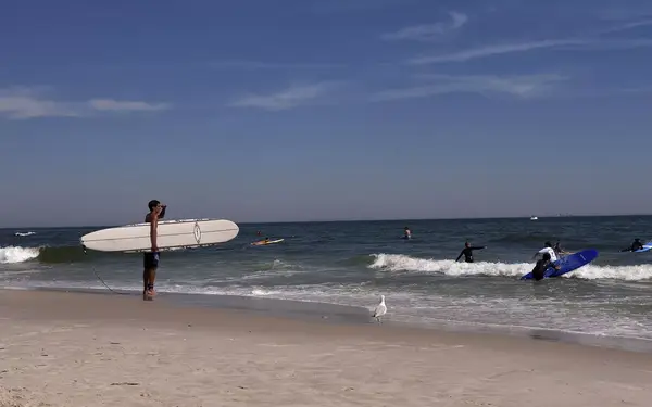 Man holding surfboard at Long Beach in New York, USA