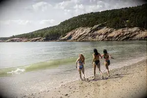 Three people walking along a sandy beach by the water