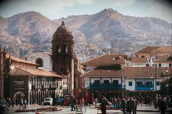 City square in Cusco with historical buildings and mountainous backdrop, people walking and gathering