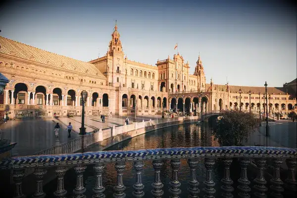 Historic building with arched colonnade and a river in front, in a plaza setting