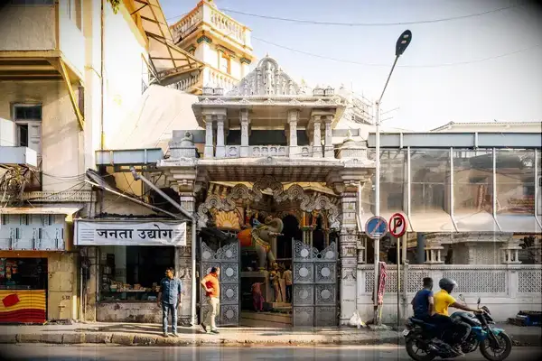 An ornate temple entrance along a street in Mumbai, with pedestrians and motorcyclists passing by