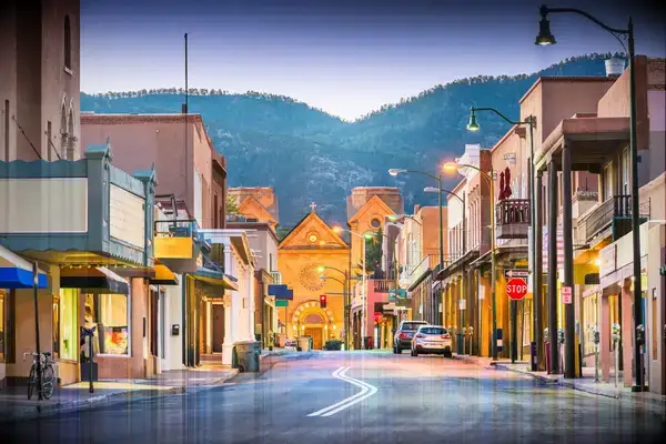 A street in Santa Fe with buildings and mountains in the background, featuring architectural styles typical of the region