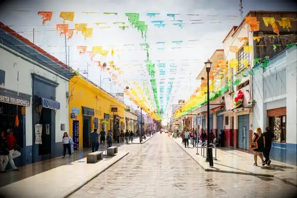 A vibrant street in Oaxaca decorated with colorful banners, lined with shops and people walking
