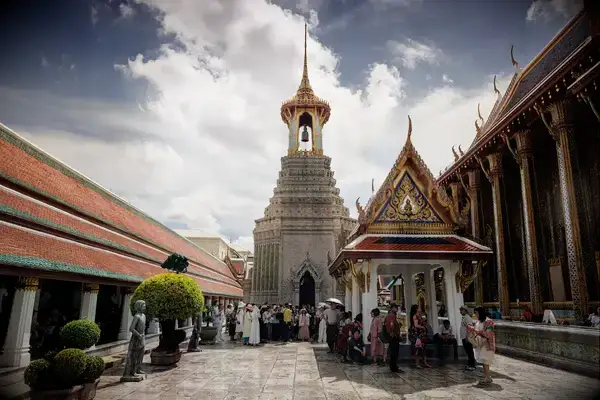 A busy courtyard in a Thai temple complex with visitors and ornate architecture