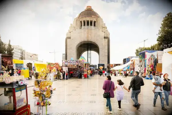 A public square near a large arched structure with street vendors and visitors
