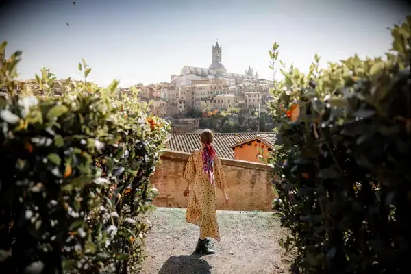 A woman walks on a path with a view of Siena, Italy in the background