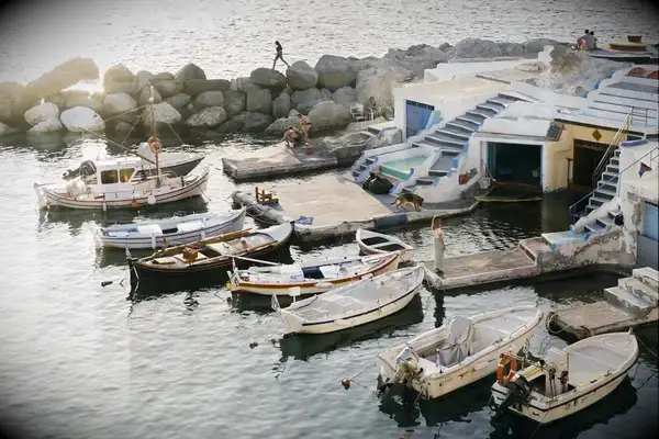 Fishing boats docked near a seaside village with stone jetties and small dwellings by the water