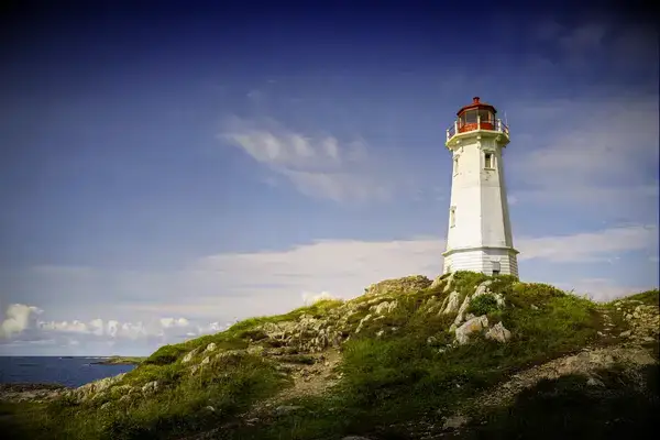 Lighthouse atop a grassy and rocky hill near the coast
