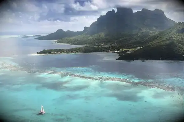 An aerial view of Bora Bora showing the lagoon, a sailboat, and mountainous terrain