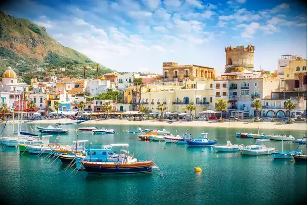A coastal town with boats docked in the water and buildings along the shore, a prominent tower visible on the right