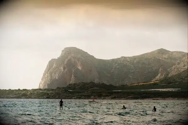 Paddle boarders and surfers in Crete at sunset