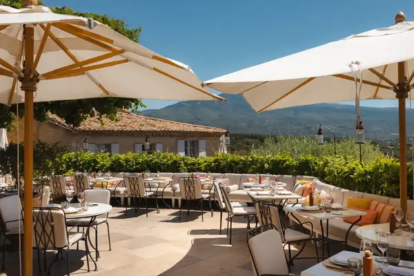 Outdoor restaurant seating area with tables and umbrellas, overlooking a scenic mountainous landscape