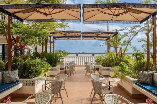 Outdoor dining area with tables and chairs under umbrellas, overlooking a seaside view