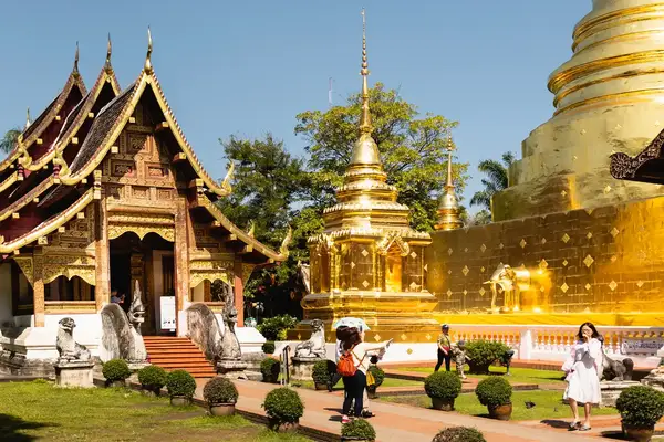 A golden Buddhist temple complex with visitors walking around