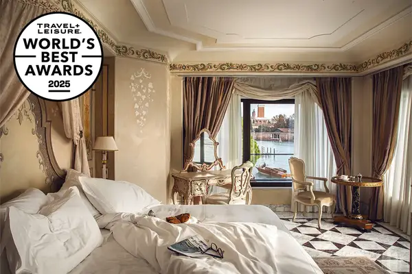 Luxurious hotel room with ornate furniture and large windows overlooking a canal in Venice