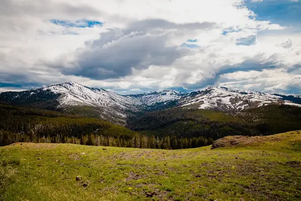 Expansive view of snow-capped mountains and forested valleys under a dynamic sky