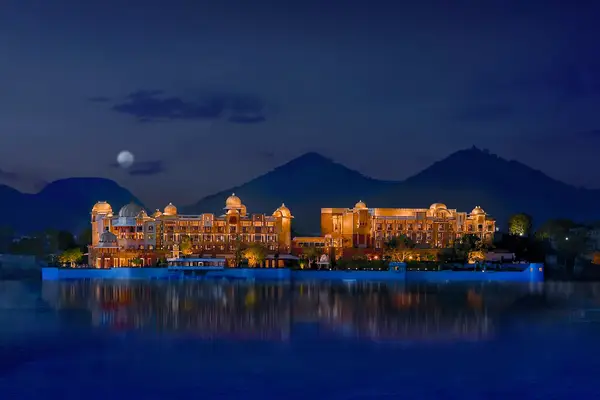 Exterior of the Leela Palace Udaipur at night with the moon and mountains rising behind