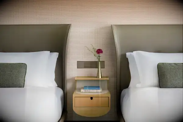 A hotel room with two twin beds, separated by a small nightstand holding books and a vase with a red flower