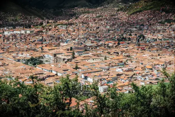 Aerial view of a city in a mountainous region, showcasing dense urban architecture and vegetation in the foreground