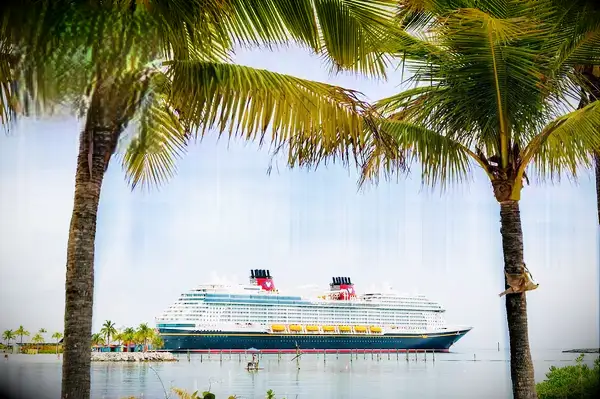 A Disney Cruise Line ship docked at a tropical location, framed by palm trees, with a Travel & Lanetrek World