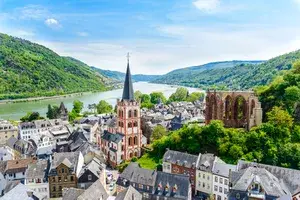 Townscape of Bacharach, Germany, showing a church with a spire, nearby ruins, and the Rhine River in the distance