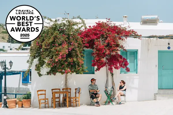 Two people sitting under flowering trees in front of a white building with blue accents