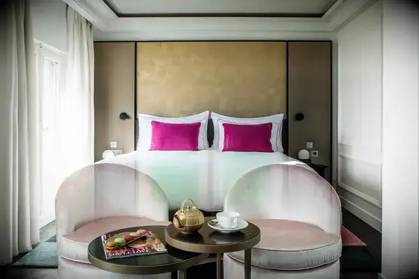 Luxurious hotel suite featuring a bed with pink pillows, armchairs, and a small table set with a teapot and cup
