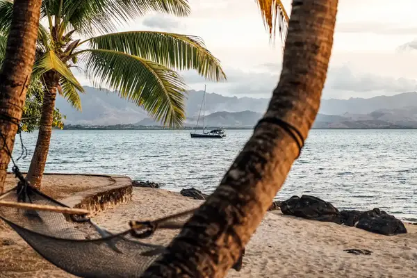 Tropical beach setting with palm trees, a hammock, and a sailboat on the water