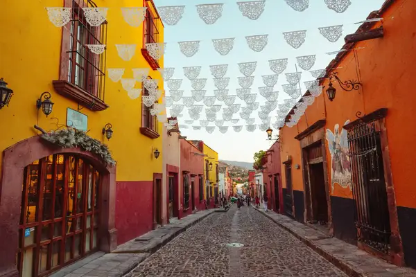 A cobblestone street in San Miguel de Allende, adorned with decorative paper banners, colorful buildings on both sides