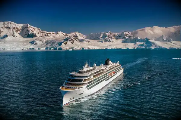 A cruise ship traveling on blue waters with a snowy mountainous landscape in the background