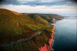 Aerial view of the Cabot Trail on Cape Breton Island, with the road winding through the forest next to the shoreline