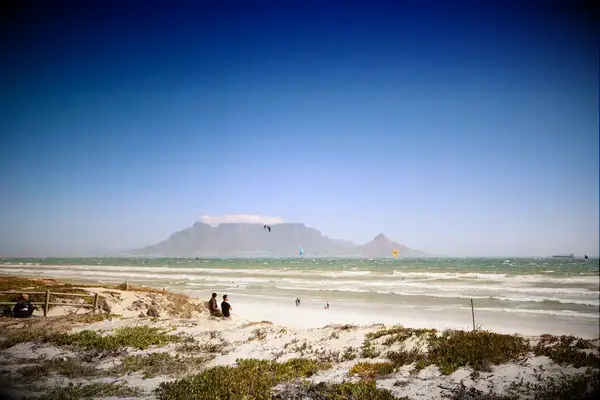 Table Mountain visible across the beach with beachgoers in the foreground and blue sky above, Cape Town, South Africa