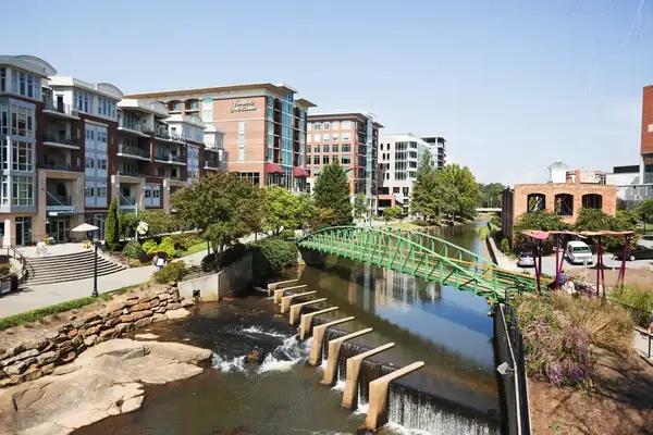 Urban scene with a river, a pedestrian bridge, and buildings in the background, featuring a parklike setting