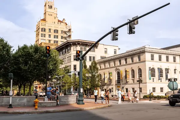 City intersection with pedestrians, historic buildings in the background, and traffic lights