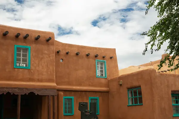 Southwestern-style adobe building with turquoise window frames and a cloudy sky backdrop