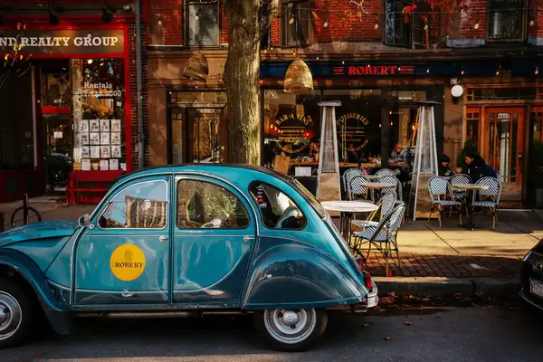 A vintage car parked on a street alongside a café with outdoor seating